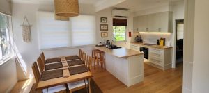 Modern open-plan kitchen and dining room with wooden floors, a split-system air conditioner above the window, and natural light streaming in.