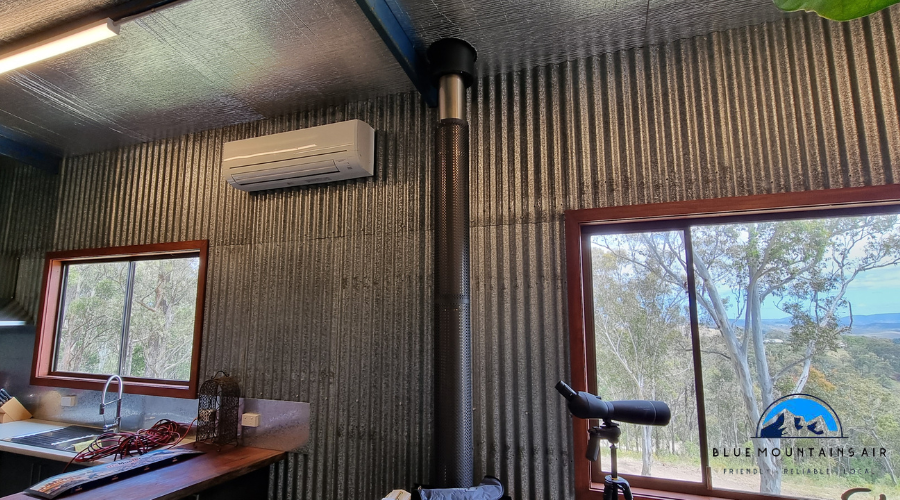 Interior of a corrugated metal cabin with a split-system air conditioner mounted on the wall above the window