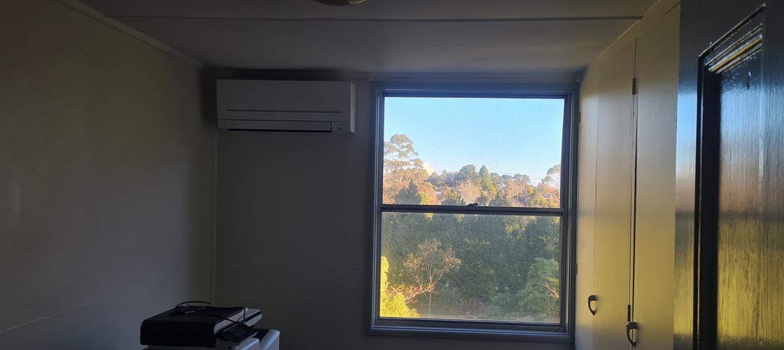Small room with a split-system air conditioner installed above a large window