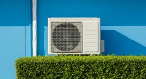 A white outdoor air conditioning unit mounted on a smooth blue wall